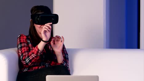 Lachende-Mädchen-auf-dem-Sofa-sitzen-und-mit-Laptop-über-virtual-Reality-Brille