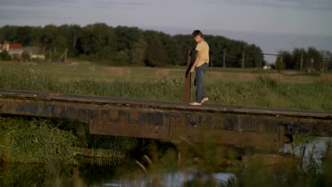 Frustrated-offended-lonely-boy-walks-along-a-bridge-near-a-river-in-countryside,-depressed-and-human-problems