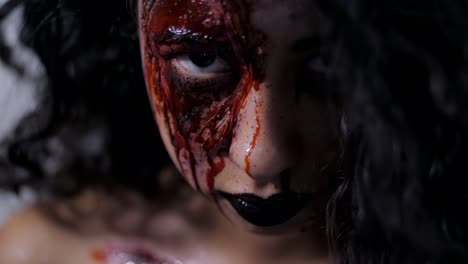 Aterrador-retrato-de-niña-con-maquillaje-de-Halloween-sangre.-Hermosa-mujer-latina-con-cabello-rizado-en-cámara-en-estudio.-Maquillaje-muerto-viviente.-Cámara-lenta