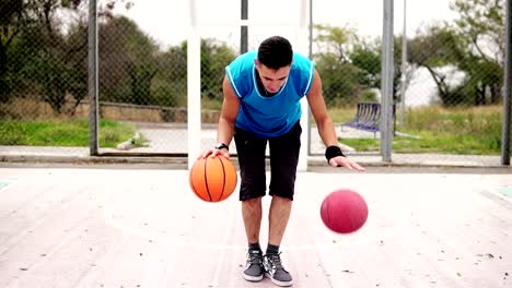 Vista-de-cerca-de-un-joven-practicando-baloncesto-en-la-cancha-de-calle.-Él-está-jugando-con-dos-bolas-simultáneamente.-Tiro-de-cámara-lenta