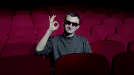 Single-man-sitting-in-comfortable-red-chairs-in-dark-cinema-theater-and-showing-ok-sign