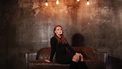 young-elegant-woman-sitting-on-a-leather-sofa-on-a-loft-wall-background