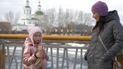 Niña-comiendo-delicioso-perro-caliente-y-hablando-con-la-madre-en-invierno