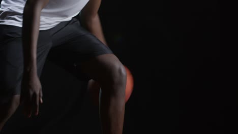 Schwarzer-Athlet-Dribbling-Basketball-auf-schwarzem-Hintergrund