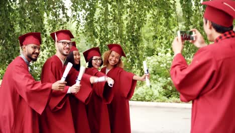 Playful-young-people-graduates-are-posing-for-photographs-making-funny-poses-and-gestures-while-their-friend-is-shooting-them-using-smartphone-camera.