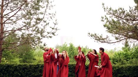 Careless-graduating-students-are-throwing-mortarboards-in-air-then-catching-them,-laughing-and-clapping-hands-celebrating-graduation.-Celebration-and-people-concept.