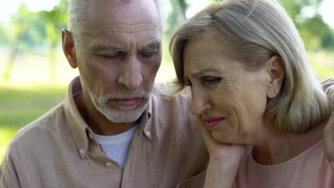 Old-woman-crying-after-horrible-news-of-cancer,-supportive-husband-sits-near