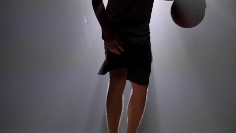 Close-shot-of-man's-legs-dribbling-ball-in-misty-room-with-floodlight