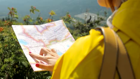 Hiker-in-a-yellow-raincoat-looking-at-map-from-mountain-top.-woman-with-map-in-mountains-FullHD