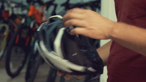 A-young-Caucasian-man-stands-near-a-stand-in-a-bicycle-store-in-the-head-protection-department.-Choosing-a-bicycle-helmet-in-a-small-store