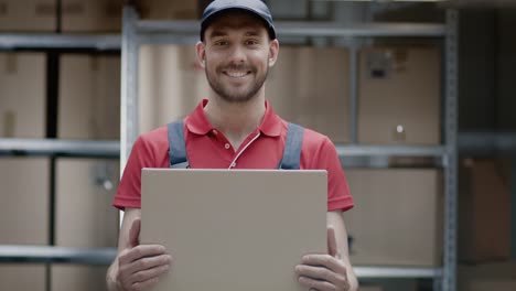 Gut-aussehend-Lagerarbeiter-in-Uniform-hält-Karton-Verpackung-und-lächelt.