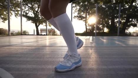 Cerca-de-un-jugador-de-baloncesto-femenino-en-golf-blanco-calcetines-y-zapatillas-azules-y-blancas,-entrenamiento-al-aire-libre-en-la-cancha,-una-bola-que-despide.-Sin-cara.-Cierre-para-arriba