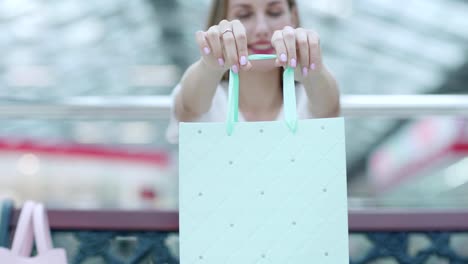 Fade-in-of-beautiful-and-happy-woman-showing-light-mint-shopping-bag-with-purchases-after-successful-shopping-in-mall