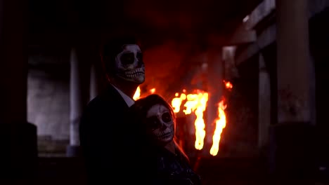 Couple-in-wedding-clothes-and-with-makeup-for-Halloween-stand-near-burning-fire