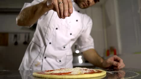 The-chef-sprinkles-spices-on-the-finished-pizza-in-the-kitchen