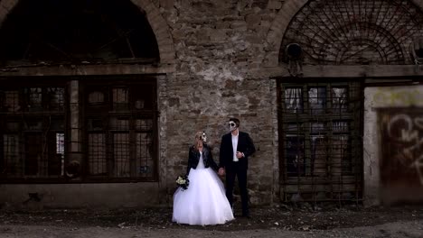 Pareja-espeluznante-en-un-vestido-de-novia-con-el-maquillaje-para-el-soporte-de-Halloween-junto-a-la-pared-de-ladrillo