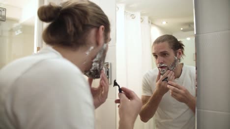 Man-Shaving-Beard-With-Razor-In-Bathroom