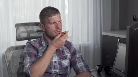 Man-eating-pizza-while-working-on-a-project-on-his-computer