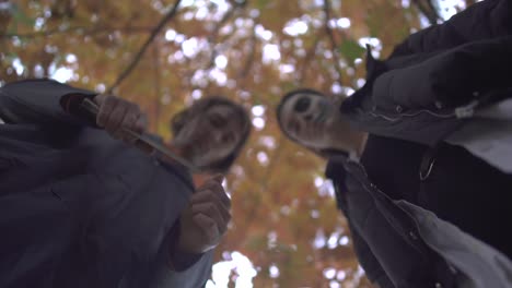 Zwei-Menschen-mit-einer-Luke-in-Halloween-Kostümen,-die-mit-ernsten-gruselnden-Gesichtern-im-Herbstpark-auf-das-Opfer-herabschauen