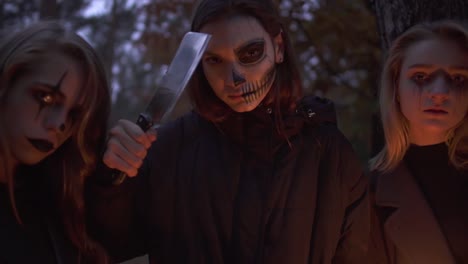 Portrait-of-three-girls-with-Halloween-makeup-on-faces-looking-in-camera-standing-in-the-forest.