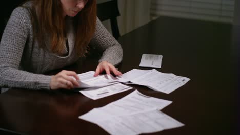 A-woman-looking-over-bills-at-the-table,-looking-stressed