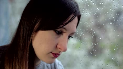 Mujer-joven-con-ausencia-de-mirada-se-sienta-húmeda-ventana-triste.-Cierre-para-arriba