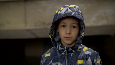 serious-boy-looks-at-the-camera-close-up,-hides-from-the-rain-in-the-tunnel