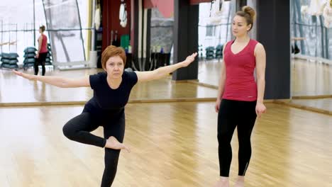 En-gimnasio-entrenador-muestra-a-la-mujer-un-ejercicio-en-la-forma-de-una-golondrina