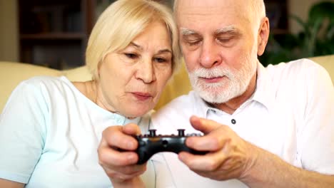 Jugadores-Senior-pareja-jugar-video-juegos-en-casa.-Jugadores-con-mando-de-consola