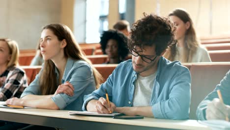 Hispanische-junger-Mann-unter-seinen-Studienfreunden-im-Klassenzimmer.-Junge-Bright-Menschen-hören-einen-Vortrag-und-nehmen-Hinweise-beim-Studium-an-der-Universität.