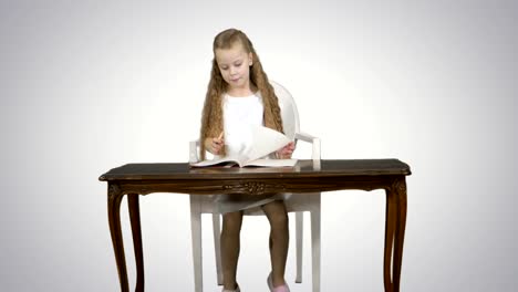 Cute-little-girl-doing-homework,-writing-down-on-white-background