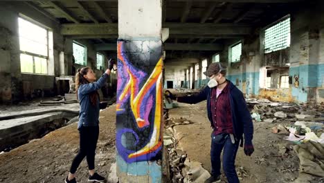 Young-people-graffiti-artists-are-using-aerosol-paint-to-decorate-abandoned-industrial-building-with-modern-graffiti-images.-Creativity,-street-art-and-people-concept.