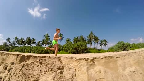 Running-little-boy-by-the-sandy-sea-beach-with-a-green-palm-trees-and-blue-sky-background-slow-motion-footage