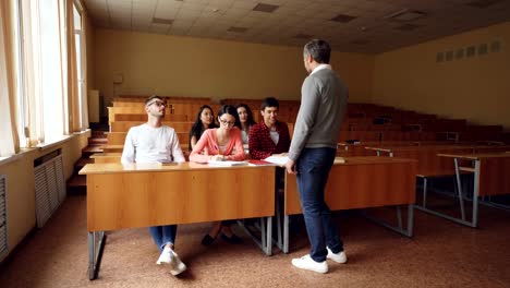 Lehrer-steht-vor-der-Tür-zum-Klassenzimmer-und-beginnt-im-Gespräch-mit-Studenten,-Vorlesung-beginnt,-Studenten-nehmen-Taxtbooks-und-Erzieher-anhören.-Lern--und-Lehrkonzept.