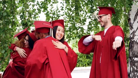 Fröhliche-Mädchen-und-jungen-Absolventen-in-Kleider-und-Hüte-sind-umarmt-einander-zur-Graduierung-gratulieren,-lachen-und-Spaß-haben.-Hochschulbildung-und-Erfolgskonzept.