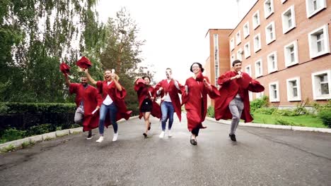 Dolly-shot-of-joyful-graduating-students-running-with-diplomas-waving-mortar-boards-and-laughing.-Higher-education,-youth-and-happiness-concept.