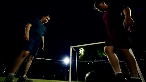 Two-young-men-alternately-kick-the-ball-on-the-field-at-night