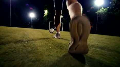 Hombre-en-zapatillas-de-deporte-camina-hacia-la-pelota-y-pone-su-pie-sobre-el-balón,-noche-en-el-campo-de-fútbol