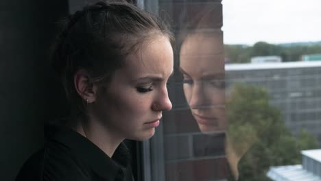 Sad-Young-Woman-Leaning-Head-Against-Glass-Window