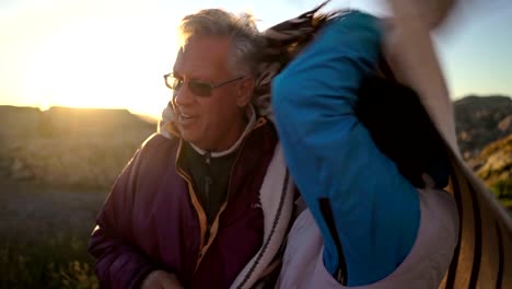 Mature-couple-at-sunset-on-the-seashore-covering-themselves-with-a-plaid-from-the-strong-wind