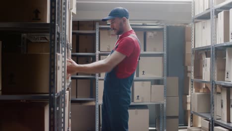 Handsome-Warehouse-Worker-Walks-into-Storeroom-with-a-Cardboard-Box-and-Puts-it-on-a-Shelf.