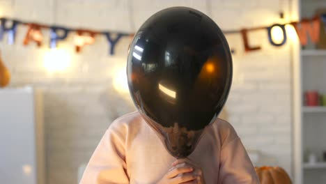 Pretty-little-child-hiding-behind-black-balloon-and-showing-claws,-Halloween