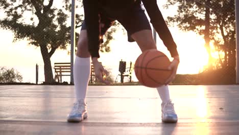 Close-up-footage-of-a-female-athlete-legs-in-white-golf-socks-and-sneakers.-Female-baasketball-player-bouncing-ball-from-hand-to-hand.-Sun-shines-on-the-background