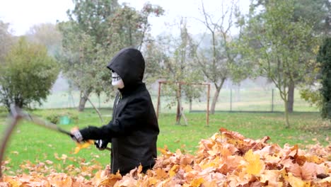 Child-boy-wearing-in-scary-Halloween-skul-skeleton-mask-holding-up-a-scythe-in-hand-cutting-leaves