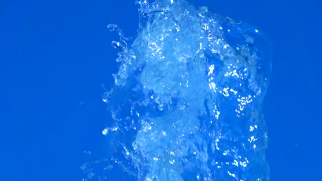 A-splash-of-clear-ice-water.-Closeup-of-light-splashing-water-in-sunny-fountain-in-park-in-summer-on-blue-sky-background.--Water-flow-of-fountain-fly-up-in-air-with-many-splashes.-Slow-motion.