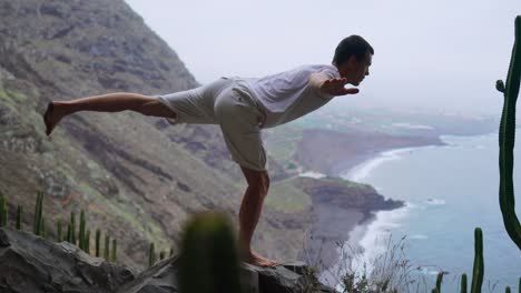 Forma-joven-practica-yoga-de-saludo-al-sol-en-la-montaña-por-mar.-Joven-disfrutando-de-la-meditación-y-el-yoga.-concepto-de-fitness,-deporte,-gente-y-estilo-de-vida---hombre-joven-haciendo-ejercicios-de-yoga