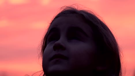 Kid-looking-up-at-the-sky-in-nature.-Little-girl-praying-looking-up-at-purple-sky-with-hope,-close-up.