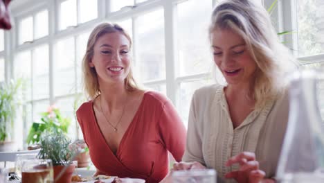 Dos-mujeres-blancas-adultos-jóvenes-comer-el-almuerzo-con-amigos-en-un-restaurante,-de-bajo-ángulo