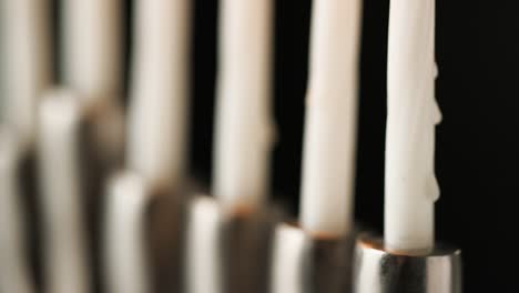 Close-up,-shallow-depth-of-field-tilt-shot-of-silver-menorah-at-an-angle,-with-white-lit-candles,-detail