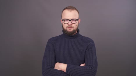 Retrato-de-hombre-joven-con-barba-y-gafas.-Mirando-a-cámara-con-ira-y-agitando-sus-brazos.-Aislado-en-fondo-gris.